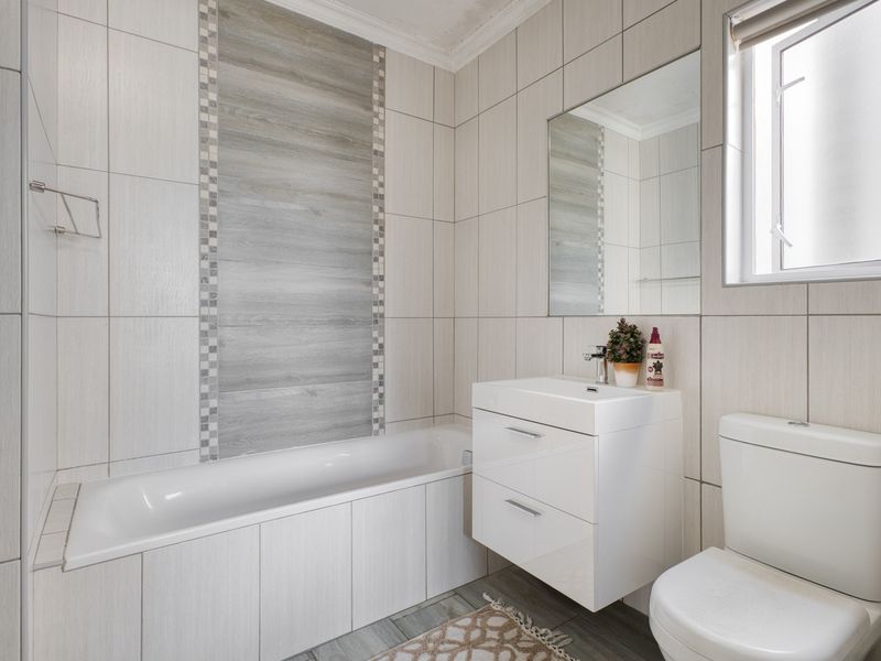 A modern, well-maintained bathroom featuring a bathtub, wall-mounted vanity with basin, toilet, and neutral tiled finishes.
