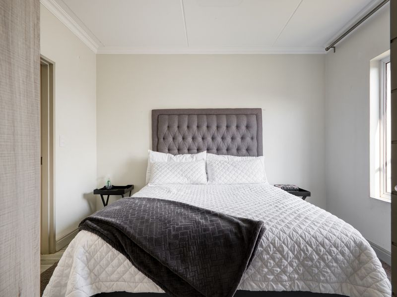 A well-maintained bedroom featuring neutral walls, crown molding, and a window with a fitted curtain rod.