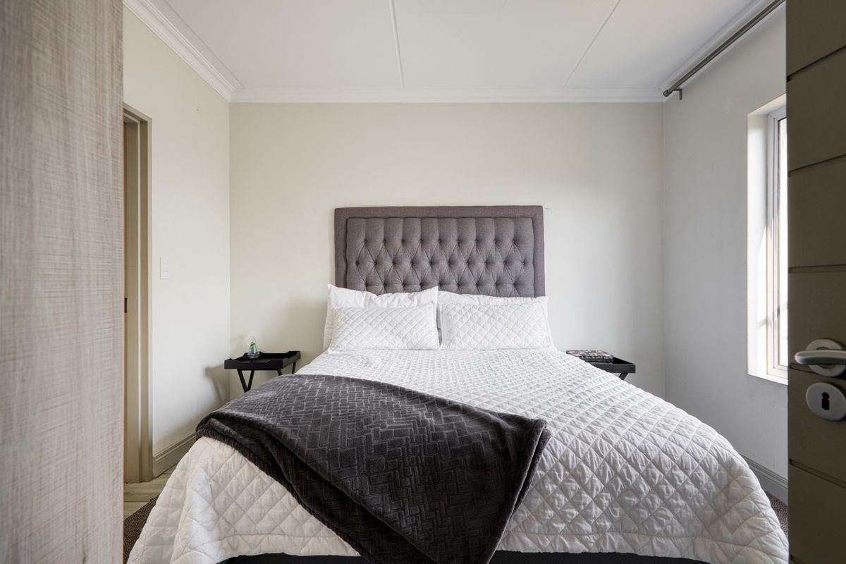 A well-maintained bedroom featuring neutral walls, crown molding, and a window with a fitted curtain rod.