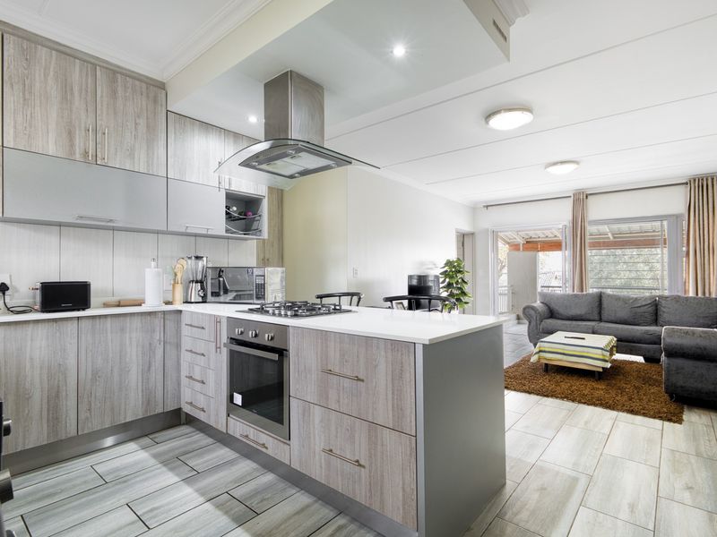 Modern open-plan kitchen and living area featuring contemporary cabinetry, integrated appliances, stone countertops, and direct access to an outdoor balcony through sliding doors.