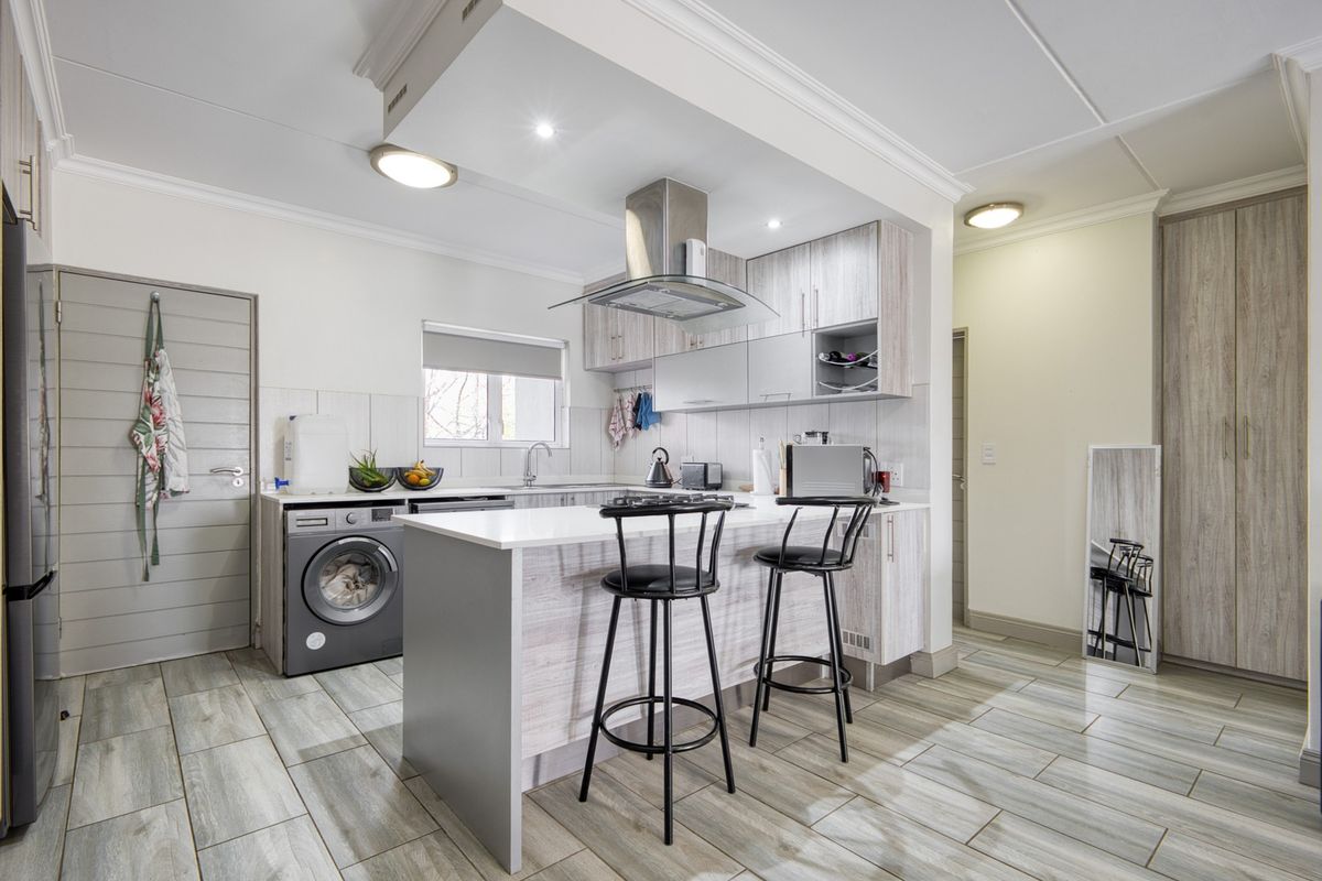 Modern kitchen featuring light wood-grain cabinetry, stone countertops, a breakfast bar, integrated stainless steel extractor fan, and durable tiled flooring.