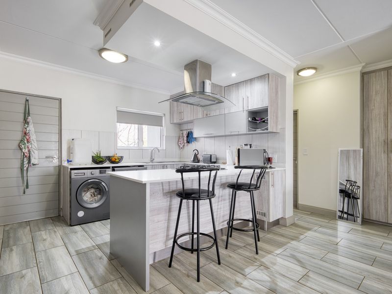 Modern kitchen featuring light wood-grain cabinetry, stone countertops, a breakfast bar, integrated stainless steel extractor fan, and durable tiled flooring.