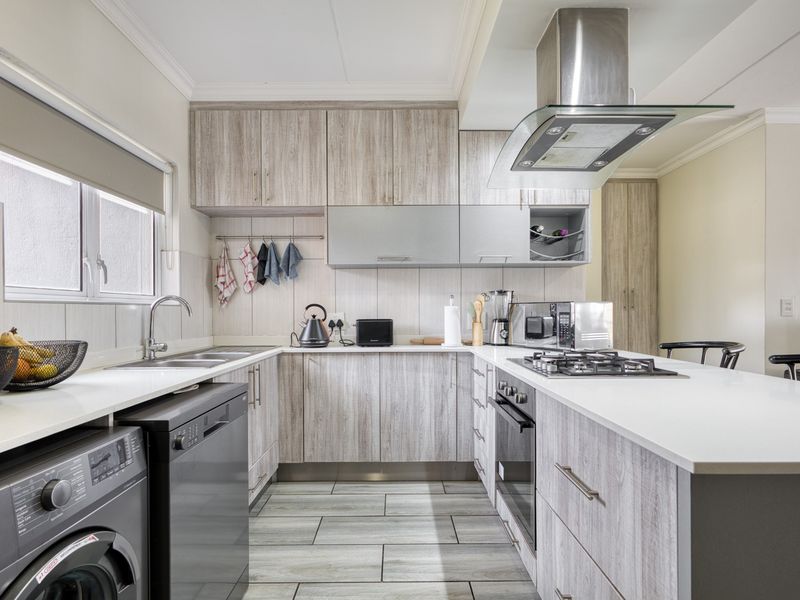 Modern kitchen featuring light wood-grain cabinetry, stone countertops, integrated gas hob, built-in oven, extractor fan, and tiled flooring with ample storage space.
