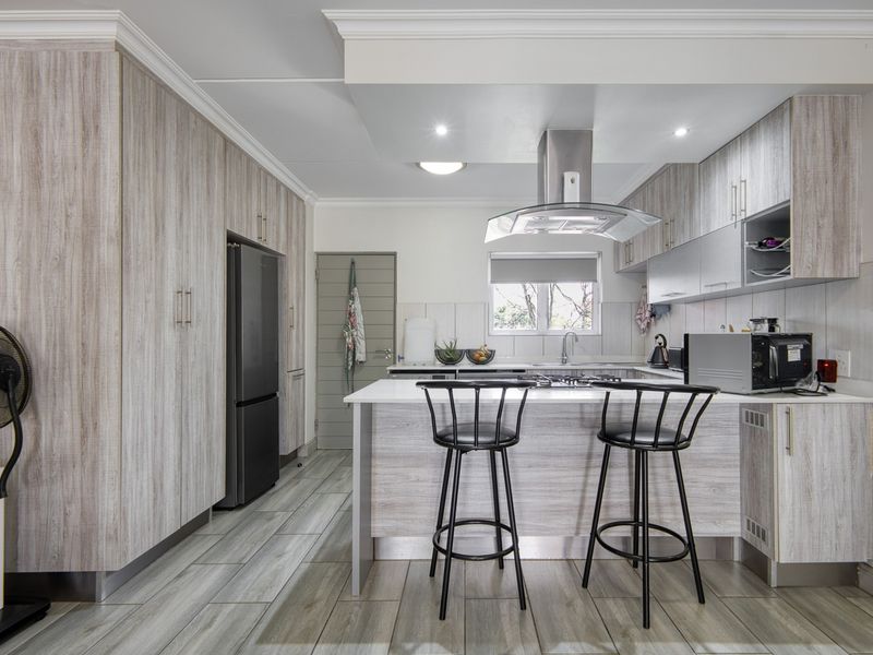 Modern kitchen featuring light wood-grain cabinetry, a central island with a built-in hob, stainless steel extractor fan, and contemporary tiled flooring.