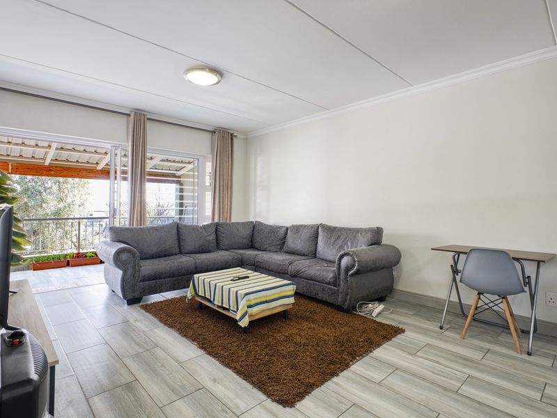 A bright living room featuring modern tiled flooring and a large sliding glass door providing access to an outdoor balcony area.