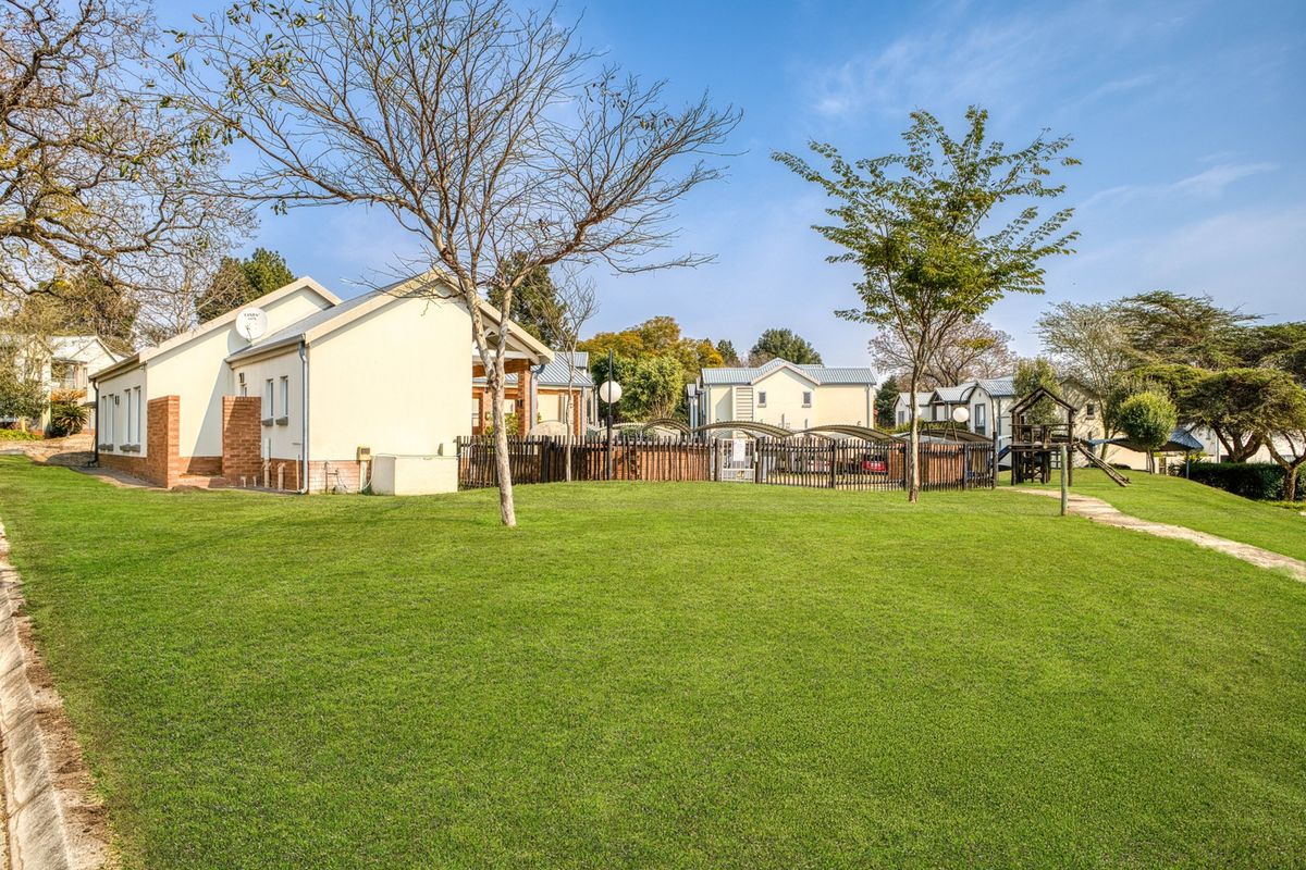 A view of the communal garden area featuring a well-maintained lawn, perimeter fencing, and paved pathways leading to the residential units.