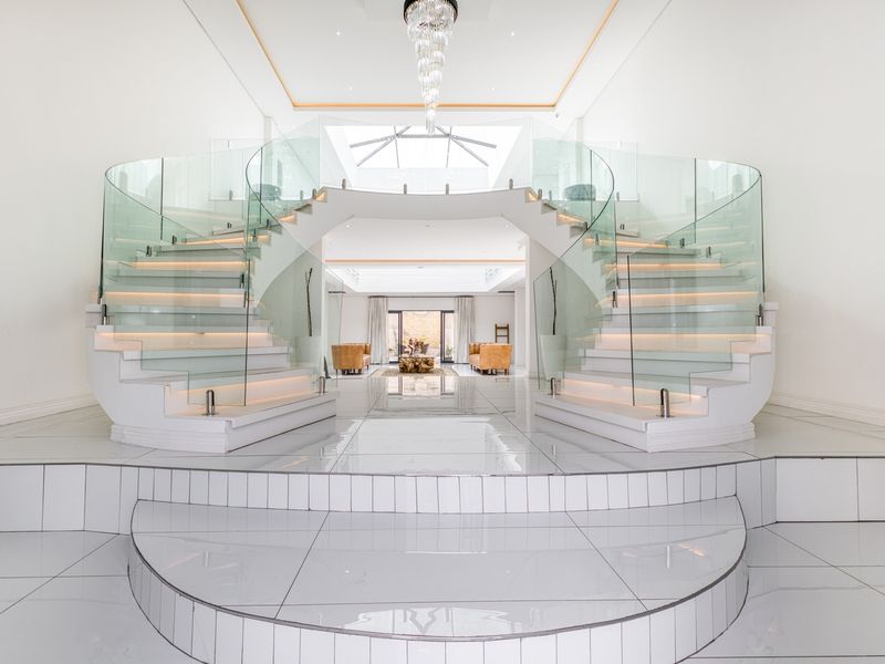 Grand entrance hall featuring a symmetrical curved staircase with glass balustrades, polished tile flooring, and a central skylight.