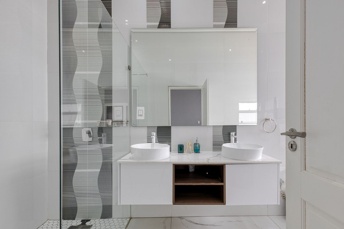 Modern bathroom featuring a sleek double vanity with vessel sinks, a large wall-mounted mirror, and a contemporary glass-enclosed shower with decorative tiled accents.