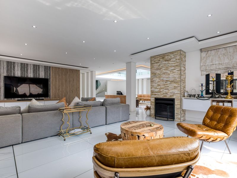 Spacious open-plan living area featuring a modern stone-clad fireplace, recessed ceiling lighting, and sleek tiled flooring with a contemporary media wall.