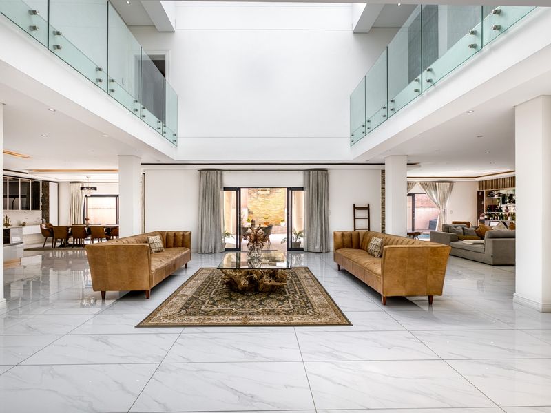 Spacious open-plan living area featuring double-volume ceilings, glass balustrades, and polished porcelain tiles, creating a bright and airy atmosphere.
