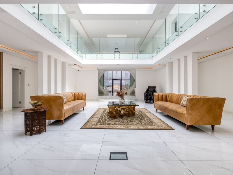 Spacious, modern living area featuring high ceilings, a large central skylight, glass balustrades, and polished marble flooring with an open-plan design.