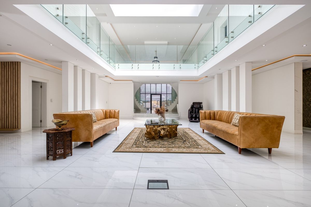 Spacious, modern living area featuring high ceilings, a large central skylight, glass balustrades, and polished marble flooring with an open-plan design.