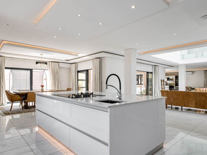 Modern open-plan living area featuring a sleek kitchen island with gas hob, high-end finishes, recessed lighting, and seamless flow to dining and lounge spaces.