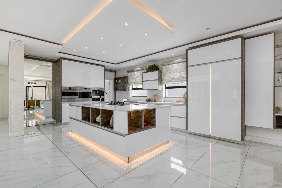 Modern, high-end kitchen featuring a large central island, integrated appliances, sleek white cabinetry, and sophisticated recessed lighting with marble-look flooring.