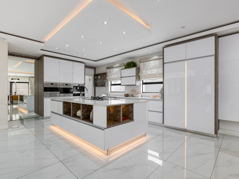 Modern, high-end kitchen featuring a large central island, integrated appliances, sleek white cabinetry, and sophisticated recessed lighting with marble-look flooring.