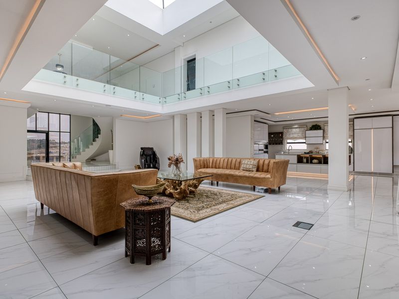 Spacious open-plan living area featuring high ceilings with a large central skylight, glass balustrades, polished marble-look flooring, and a modern integrated kitchen.