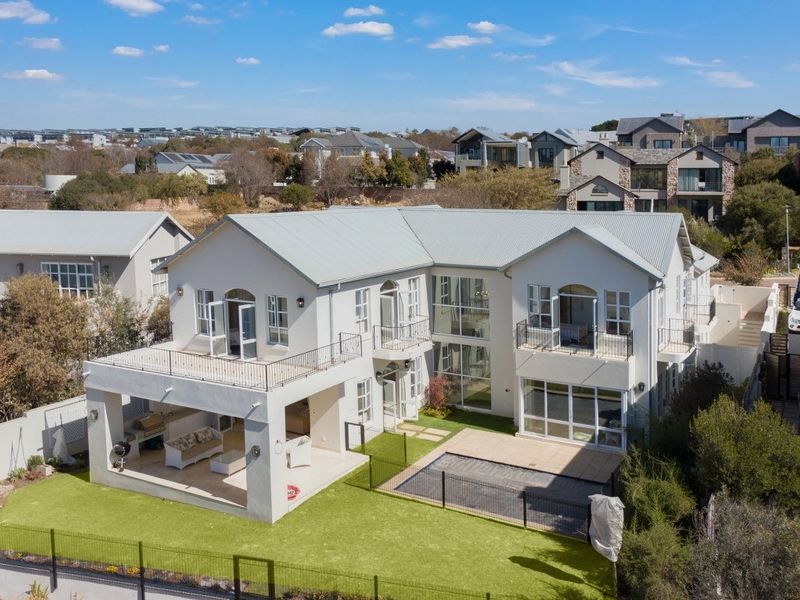 Aerial view of a modern double-story residence featuring a covered patio, balcony, swimming pool, and landscaped garden area.