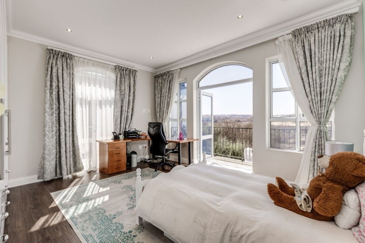 Spacious bedroom featuring laminate flooring, recessed lighting, and arched glass doors opening onto a private balcony with scenic views.