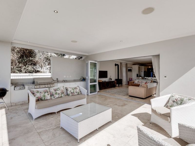 Spacious covered patio featuring stone flooring, recessed lighting, and a built-in braai area, seamlessly connecting to the indoor living space through large stacking doors.