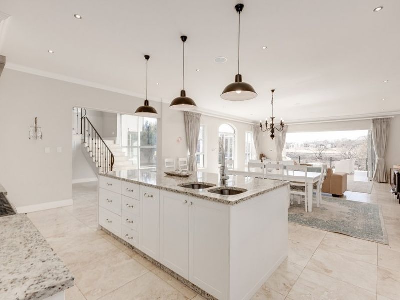 Spacious open-plan kitchen and living area featuring a large granite-topped island, modern pendant lighting, and seamless flow to the dining space and staircase.
