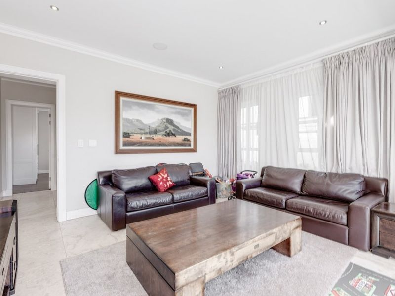 A bright and well-maintained living room featuring neutral tiled flooring, recessed downlighting, and elegant crown molding.