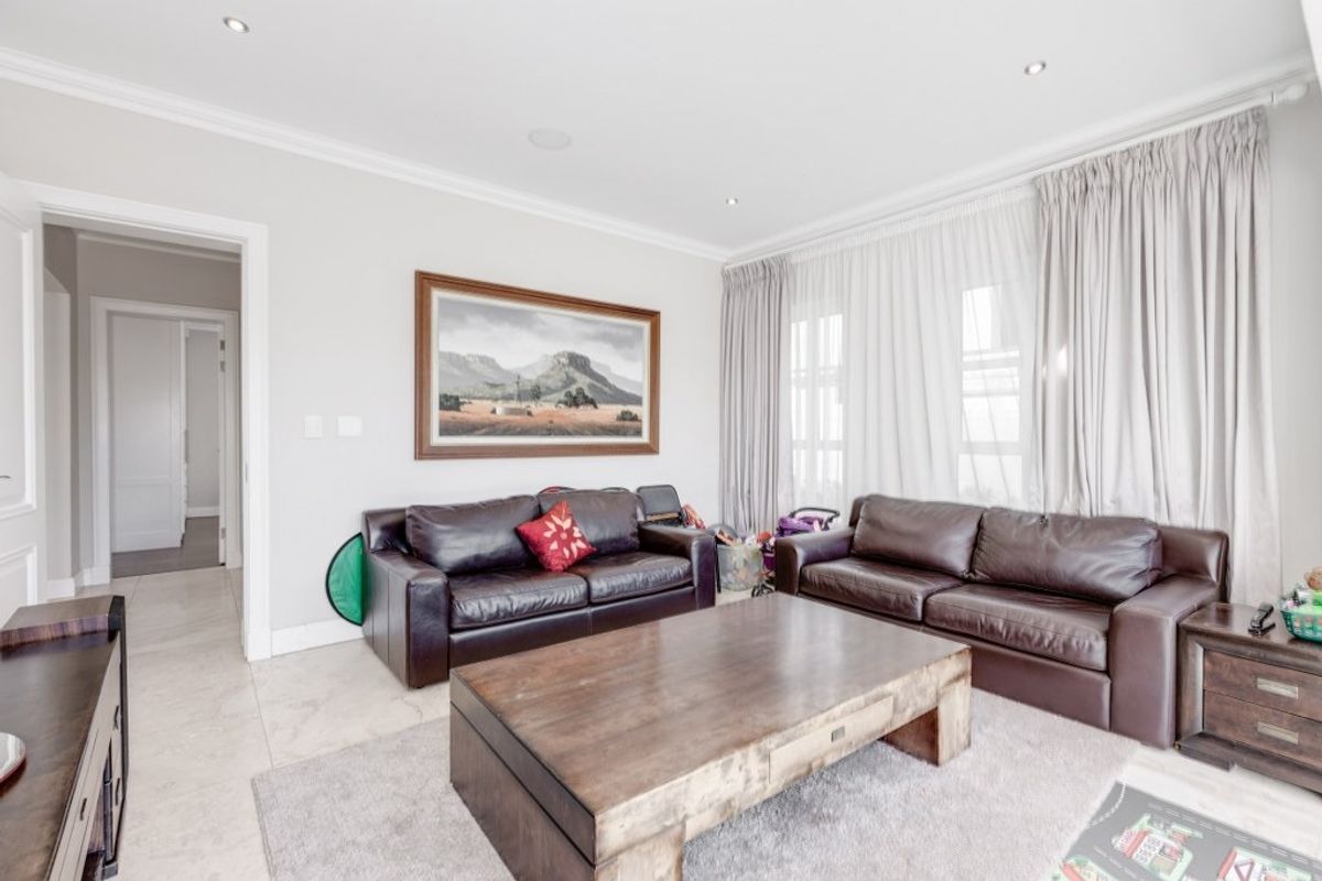 A bright and well-maintained living room featuring neutral tiled flooring, recessed downlighting, and elegant crown molding.