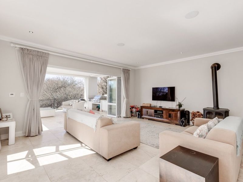 Spacious open-plan living area featuring tiled floors, a cozy fireplace, and seamless flow through bi-fold doors to an outdoor patio with a built-in braai.