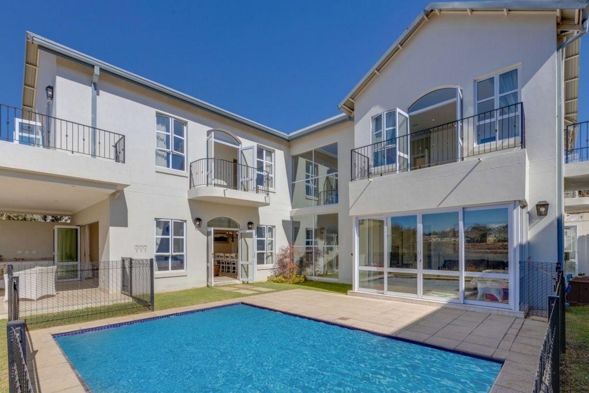 Rear elevation of a two-story house featuring a swimming pool, paved deck, multiple balconies with wrought iron railings, and large glass sliding doors.