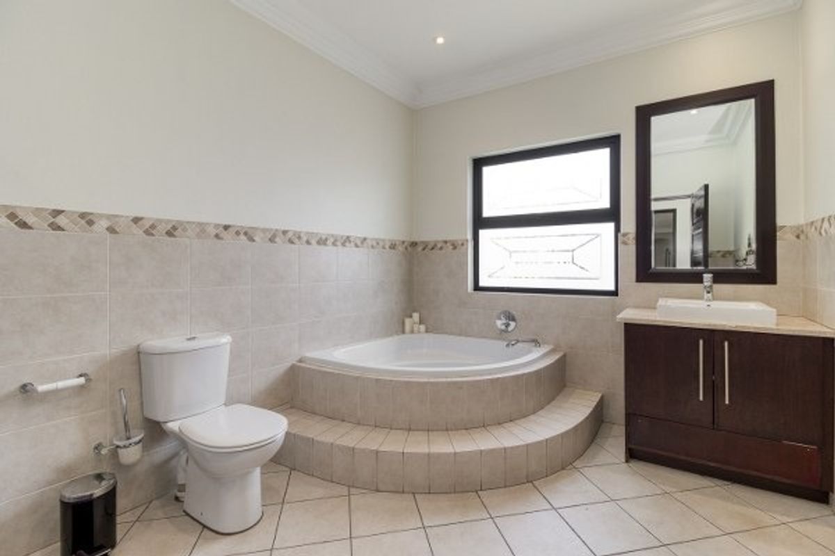 A well-maintained bathroom featuring a raised corner bathtub, a dark wood vanity with a vessel sink, and neutral tiled finishes.