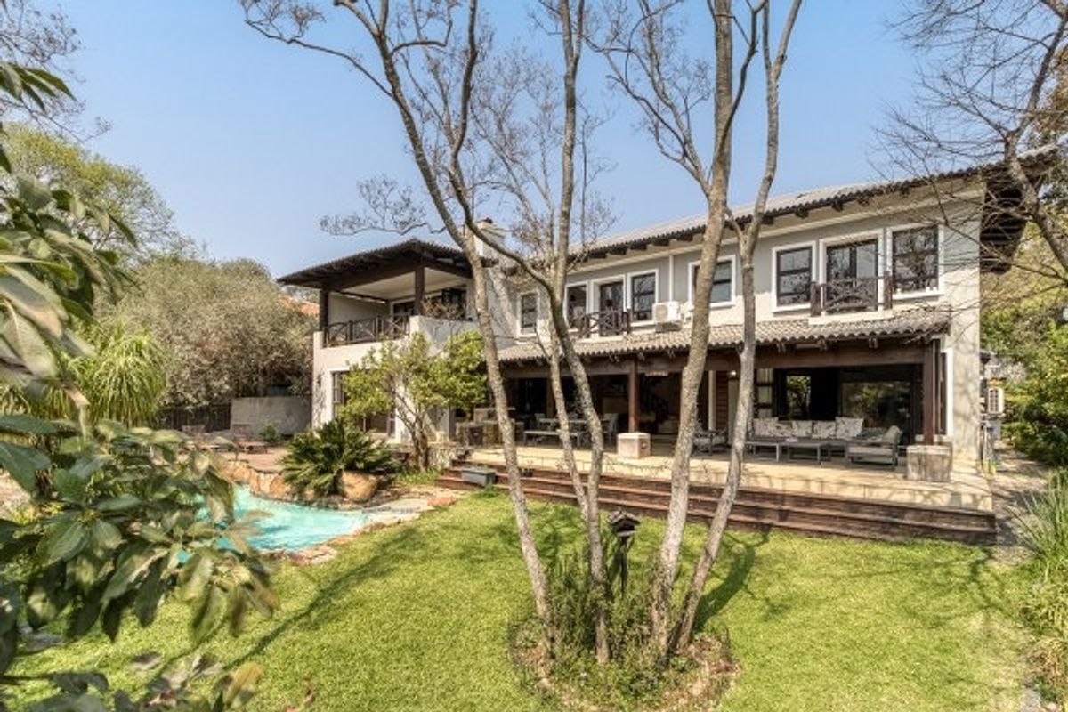 Rear view of a two-story house featuring a swimming pool, expansive covered patio, timber decking, and a well-maintained garden.