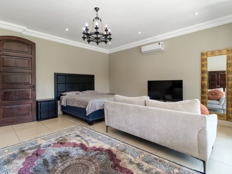 Spacious bedroom featuring tiled flooring, a decorative chandelier, cove cornicing, and a wall-mounted split-system air conditioner.