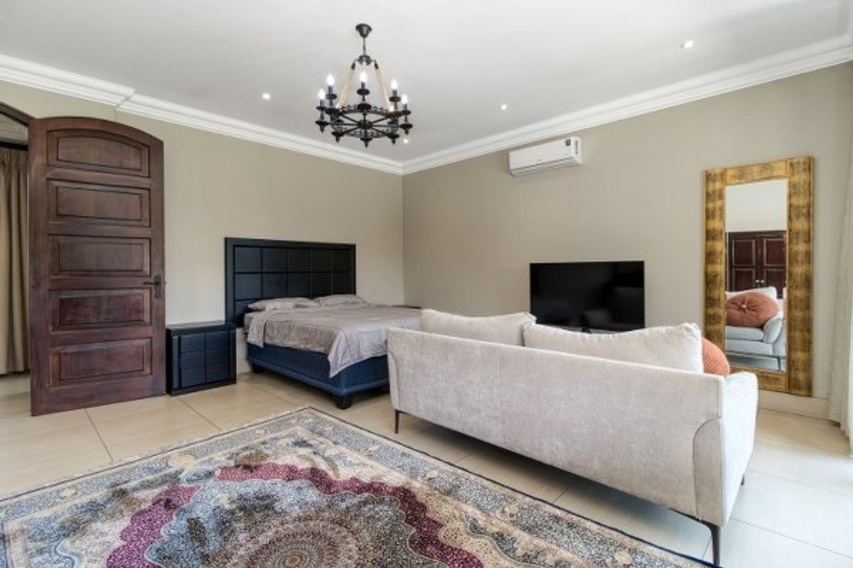Spacious bedroom featuring tiled flooring, a decorative chandelier, cove cornicing, and a wall-mounted split-system air conditioner.