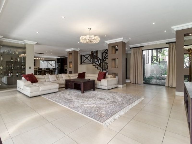 Spacious open-plan living area featuring tiled floors, recessed lighting, built-in display niches, and a staircase, with seamless access to the outdoor patio.