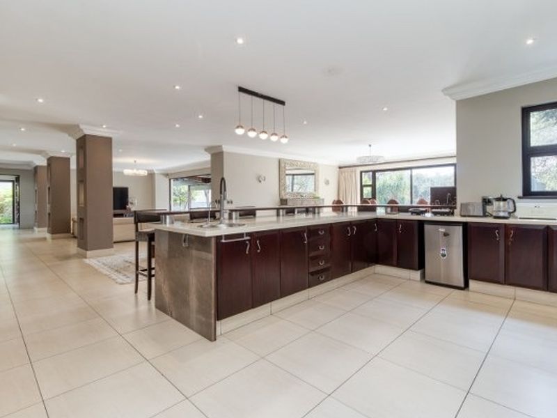 Spacious open-plan kitchen featuring dark wood cabinetry, a large central island with breakfast bar, and neutral tiled flooring throughout the living area.
