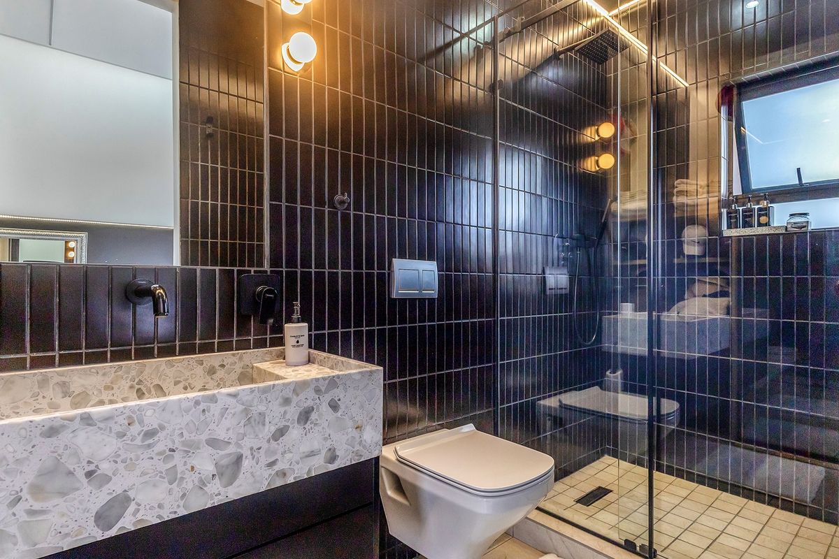 Modern bathroom featuring dark vertical wall tiles, a terrazzo vanity countertop, wall-mounted fixtures, and a glass-enclosed walk-in shower.