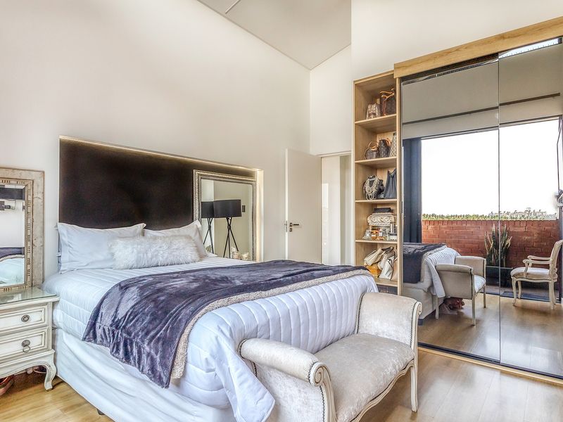 Modern bedroom featuring high ceilings, built-in mirrored wardrobes with integrated shelving, and direct access to a private balcony.
