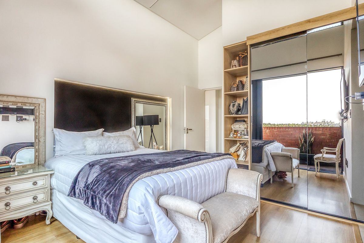 Modern bedroom featuring high ceilings, built-in mirrored wardrobes with integrated shelving, and direct access to a private balcony.