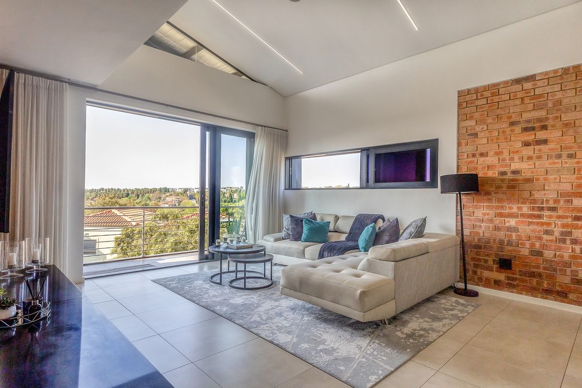 Modern living room featuring a striking exposed brick wall, high raked ceilings with linear lighting, and large sliding doors opening to a balcony with views.
