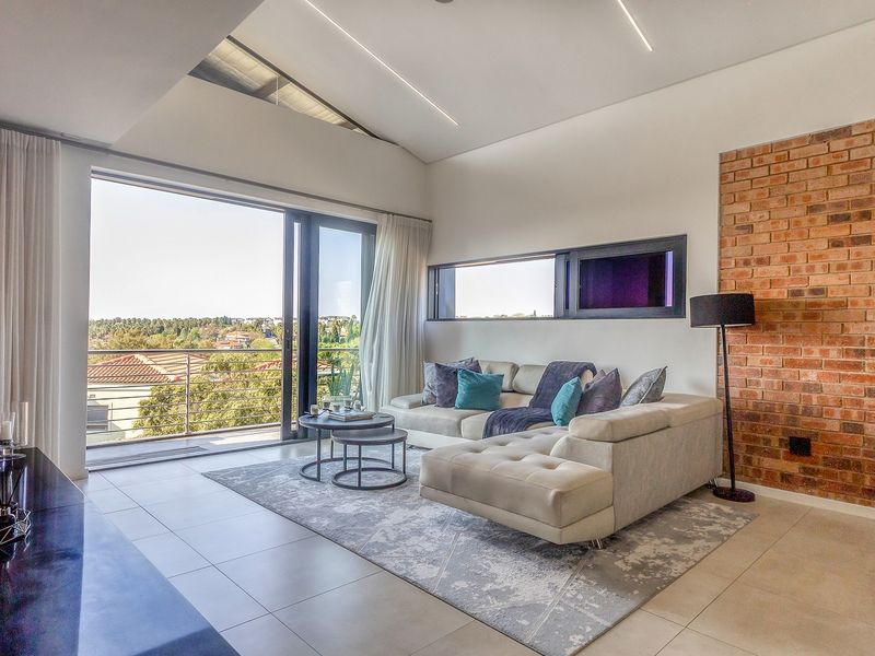 Modern living room featuring a striking exposed brick wall, high raked ceilings with linear lighting, and large sliding doors opening to a balcony with views.