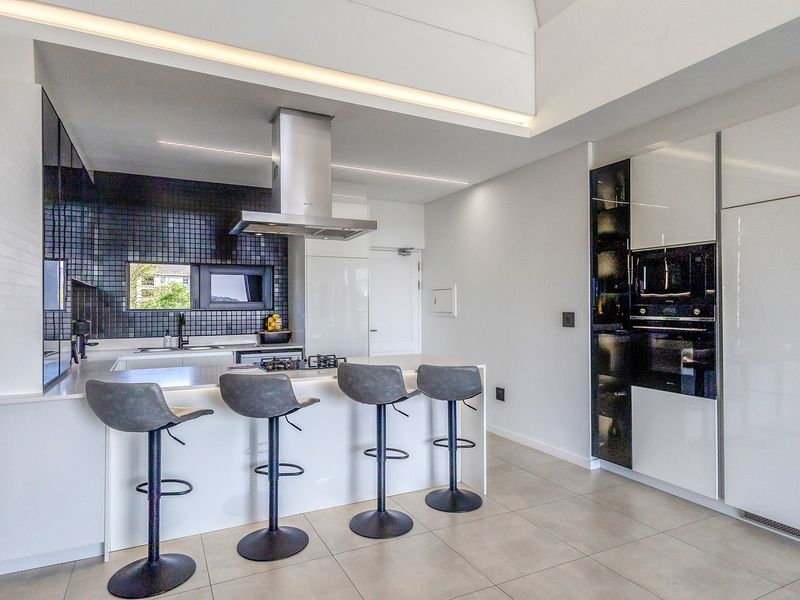 Modern kitchen featuring a central island with gas hob, sleek cabinetry, integrated appliances, and a stylish black tiled backsplash.
