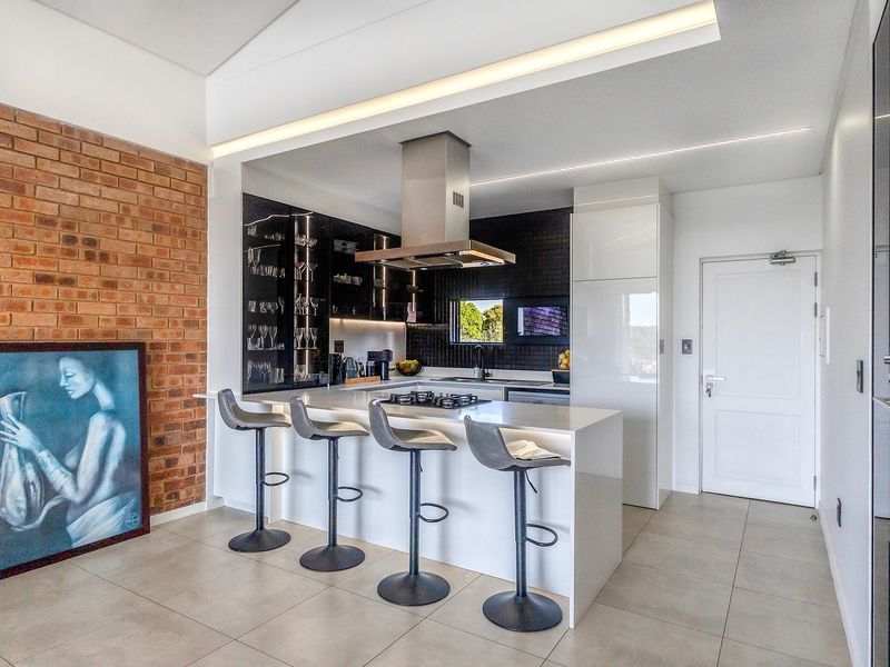 Modern kitchen featuring a central island with gas hob, sleek cabinetry, stone countertops, and an exposed brick feature wall with integrated lighting.