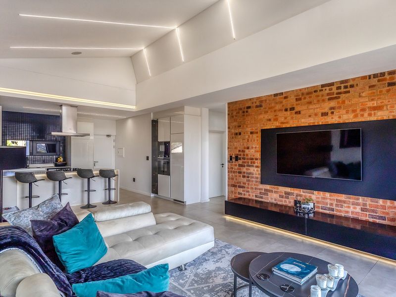 Modern open-plan living area featuring a striking exposed brick feature wall, vaulted ceilings with integrated LED lighting, and a sleek, contemporary kitchen.