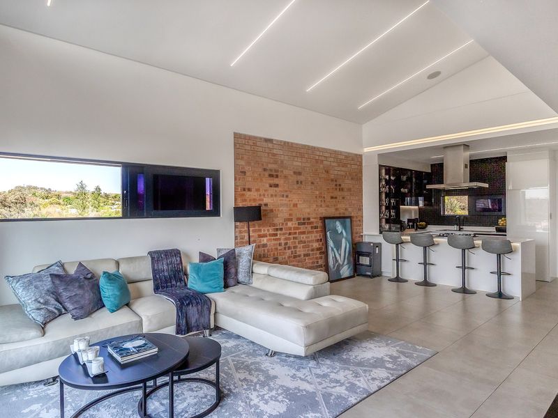 Modern open-plan living area featuring a vaulted ceiling, exposed brick accent wall, and a sleek kitchen with a central island and integrated lighting.