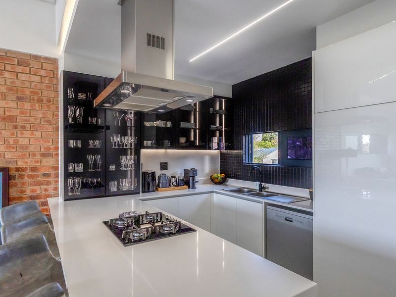 Modern kitchen featuring sleek white cabinetry, quartz countertops, a gas hob, integrated appliances, and a stylish exposed brick feature wall.