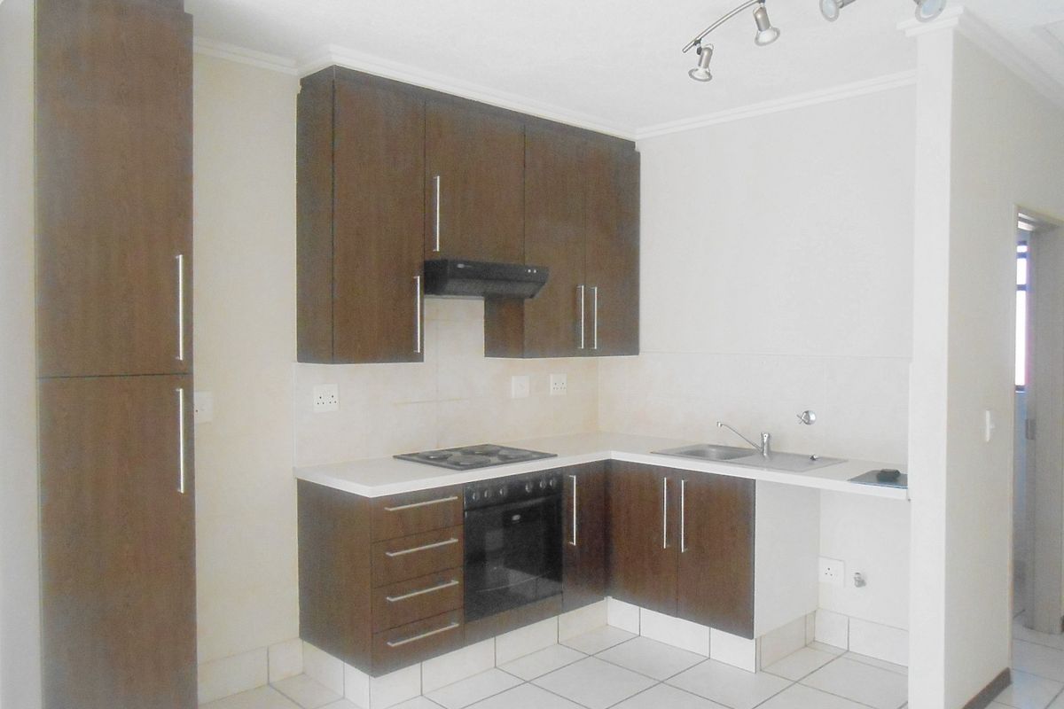 A clean, functional kitchen featuring dark wood cabinetry, built-in oven and hob, stainless steel sink, and neutral tiled flooring.