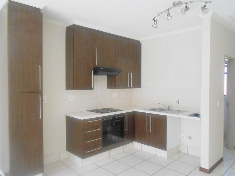 A clean, functional kitchen featuring dark wood cabinetry, built-in oven and hob, stainless steel sink, and neutral tiled flooring.