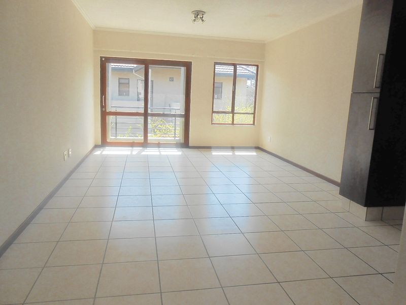 An empty open-plan living area featuring neutral tiled flooring, built-in cabinetry, and natural light through a sliding glass door and window.