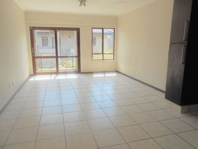 An empty open-plan living area featuring neutral tiled flooring, a sliding glass door leading to a balcony, and built-in cabinetry.