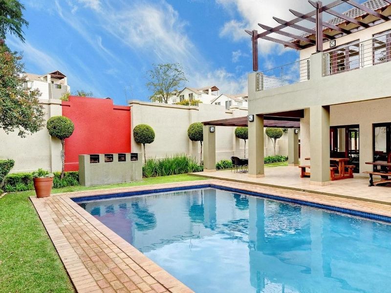 A well-maintained outdoor area featuring a swimming pool, brick coping, a covered patio with a timber pergola, and a built-in braai.