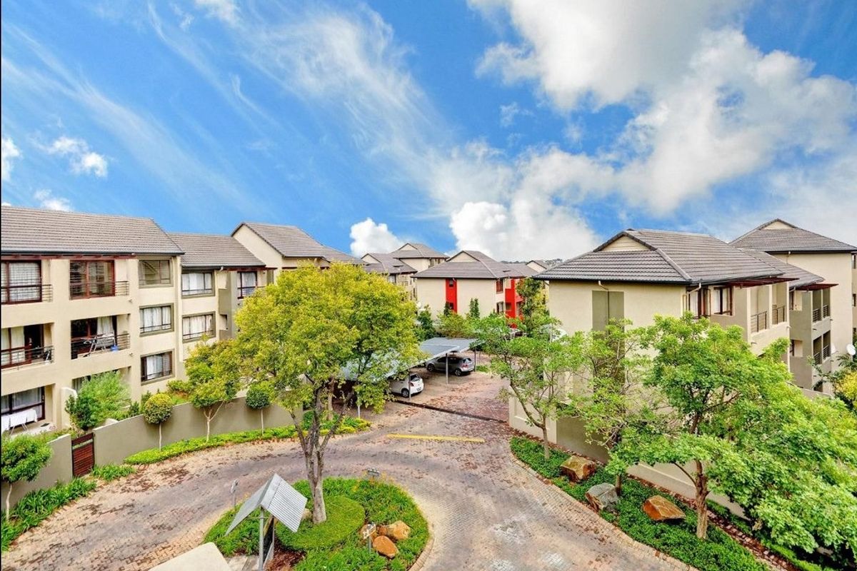 An elevated aerial view of the apartment complex grounds, featuring paved driveways, landscaped gardens, and covered parking areas.